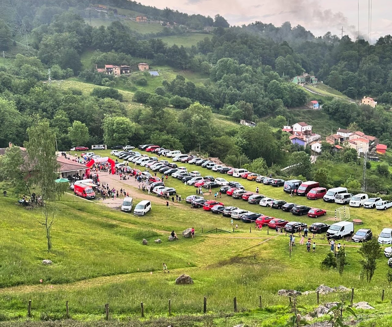 El Área Recreativa de Lantero desde lo alto del prado, con la zona de salida y meta, el arco hinchable rojo y el público