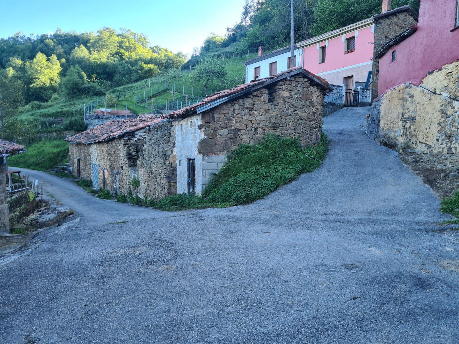 Calle de Aragustín con una casa de piedra y, al fondo, los edificios rosa y rojo entre los que empieza el sendero